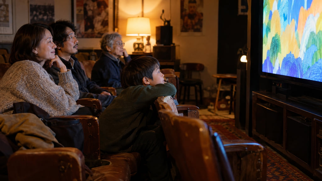 A child, two parents, and an older adult watching abstract animation in a small screening room.