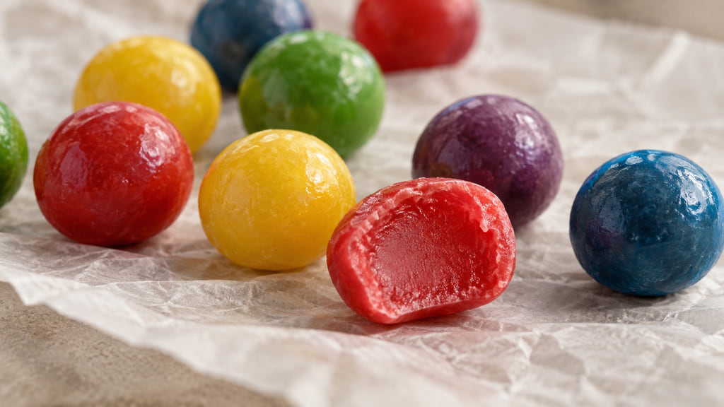 Multicolored round chewy candies with one red piece cut open to show a soft center.
