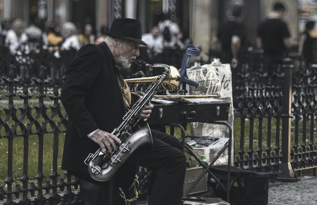 Man Sitting on Stool While Playing Saxophone Beside Fence